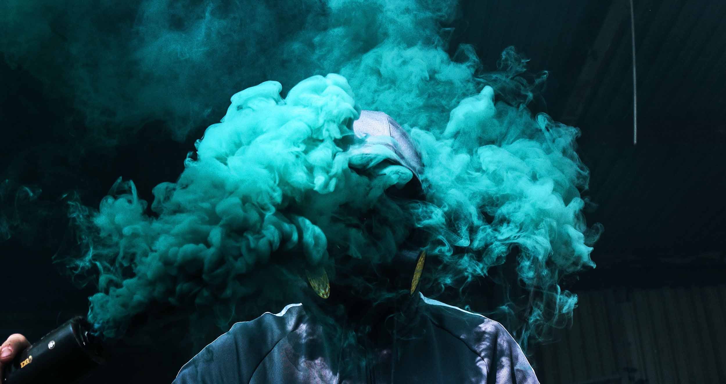 Hooded person projecting teal smoke in front of head Image by Tom Roberts (dsQEmEfKuFg on unsplash.com)